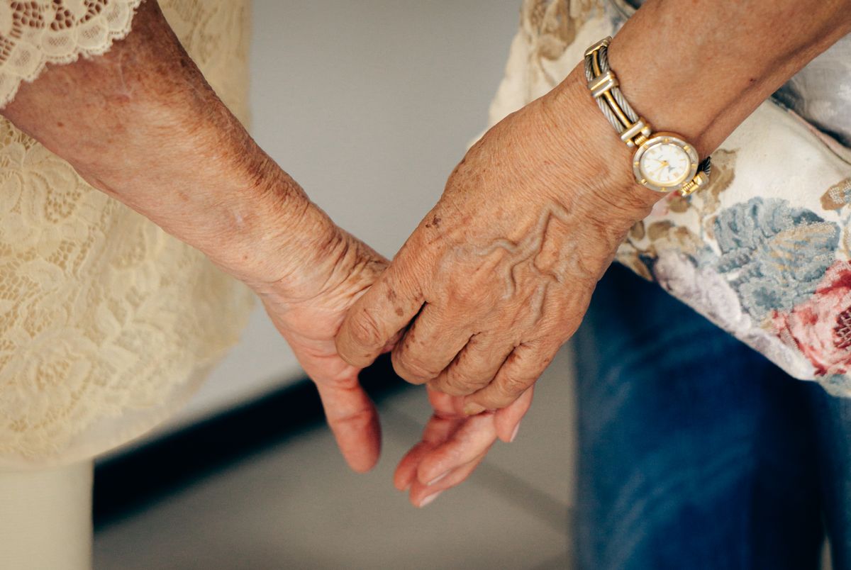 Two older hands clasped together on a table